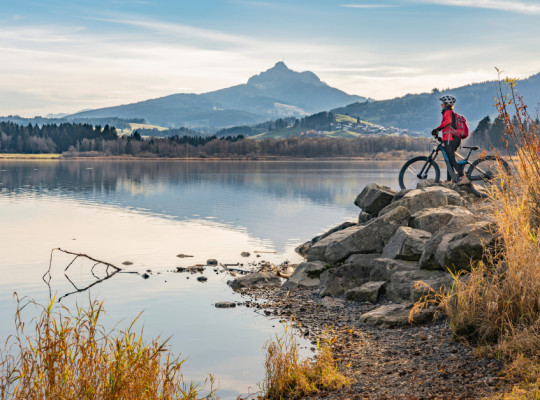 Foto eines Sees mit Bergpanorama und Mountainbiker im rechten Bildrand